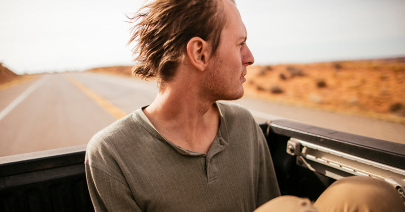 Young man rides in truck bed with wind blowing his hair