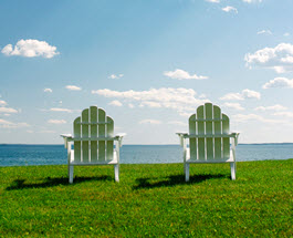 Two muskoka chairs facing a lake.